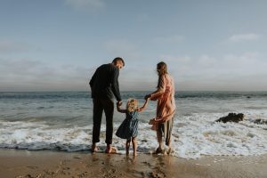 Parents tenant les mains de leur petite fille blonde au bord de l'océan