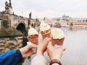 Trois mains tenant un cornet de glace face à un pont à Prague