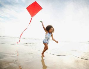 Petite fille jouant sur la plage avec son cerf-volant rouge déployé grâce au vent