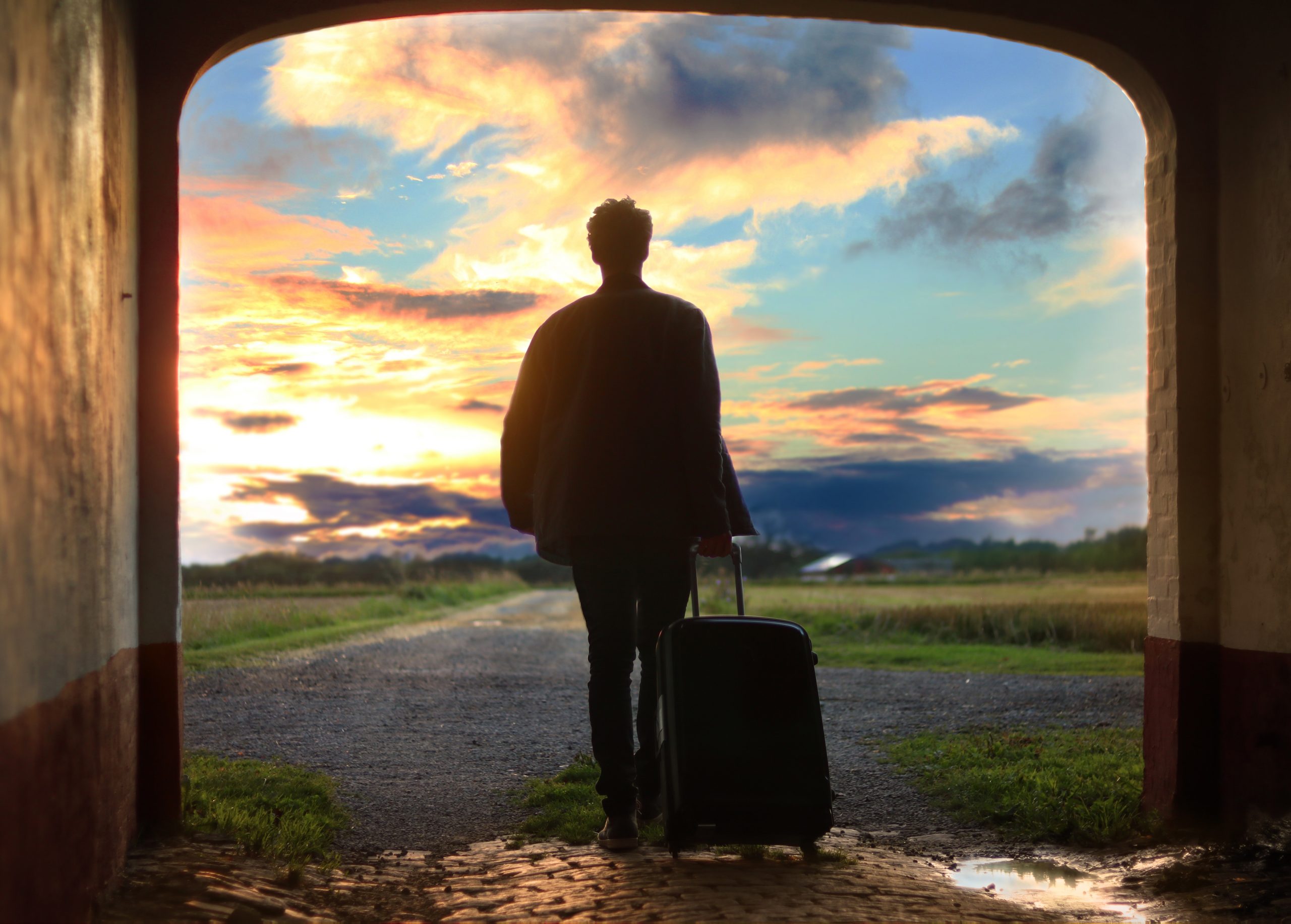 Homme de dos tenant sa valise de voyage face à un coucher de soleil