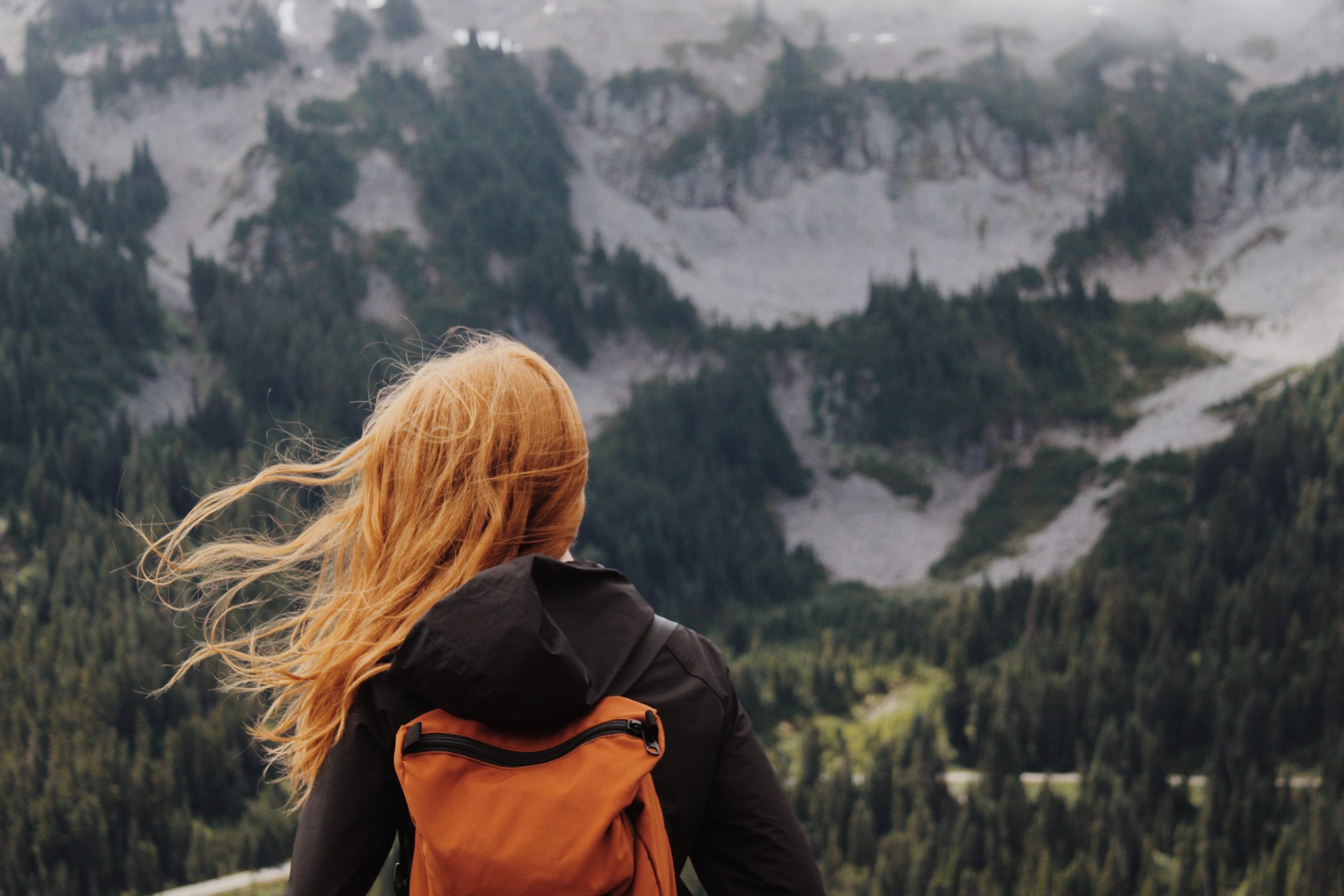 Jeune femme avec un sac à dos de voyage face à un paysage de montagne
