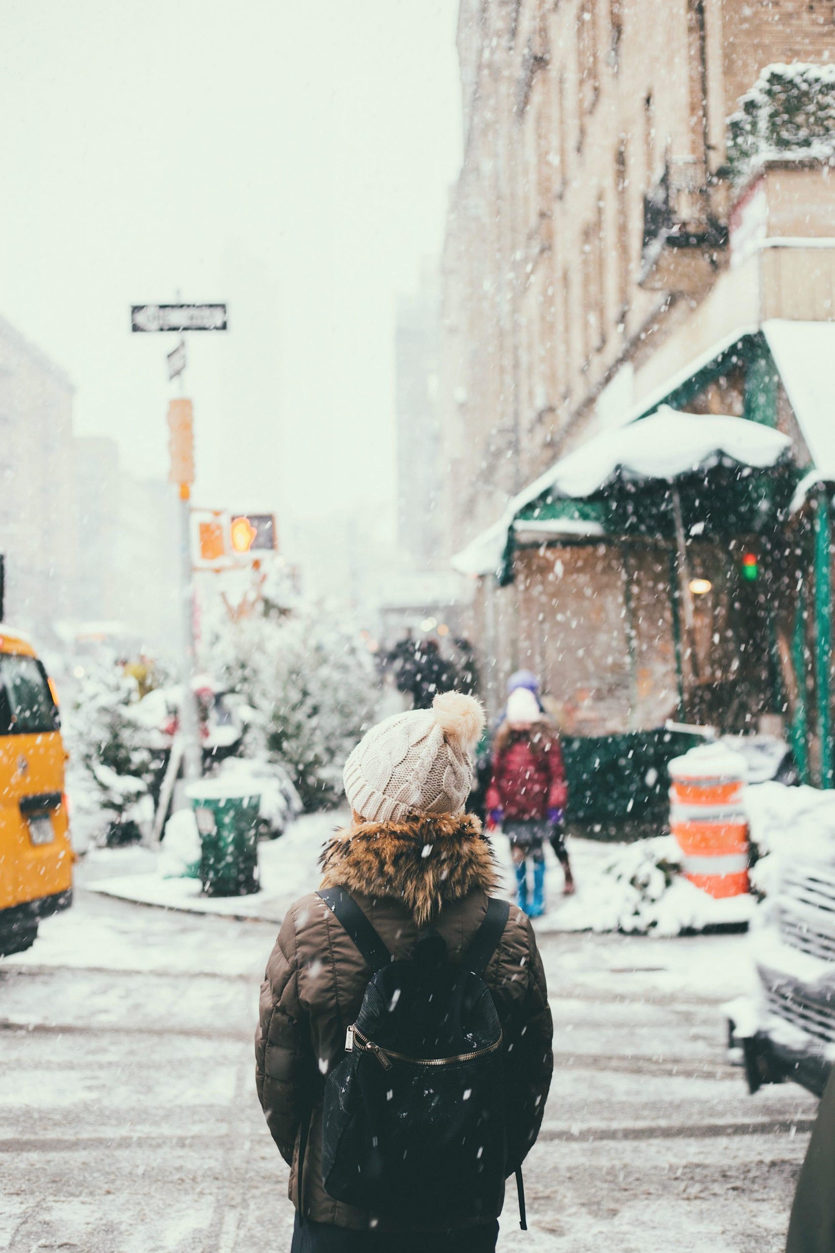femme portant un bonnet un manteau d'hiver et un sac à dos se tenant dans la rue pendant que la neige tombe